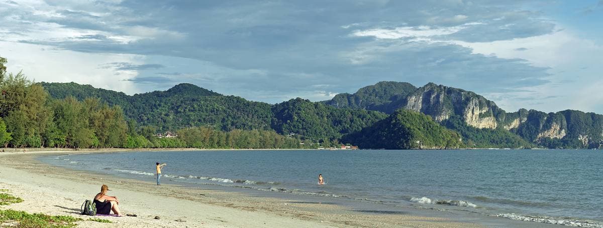 A long flat beach under casuarina trees with limestone islands offshore