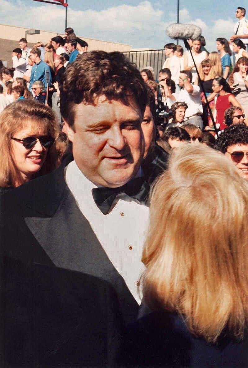 John Goodman in a dinner jacket among a crowd on a sunny red carpet