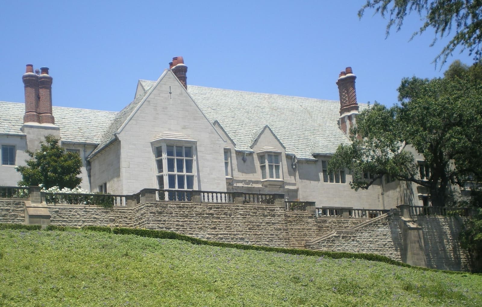 A grey stone Tudor-style mansion with tall chimneys above a lawn