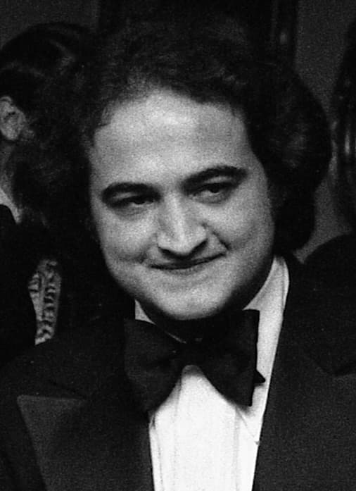 John Belushi in black tie, smiling sideways, in a black-and-white photograph