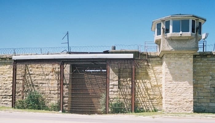 A barred gate in a limestone prison wall beneath a watchtower