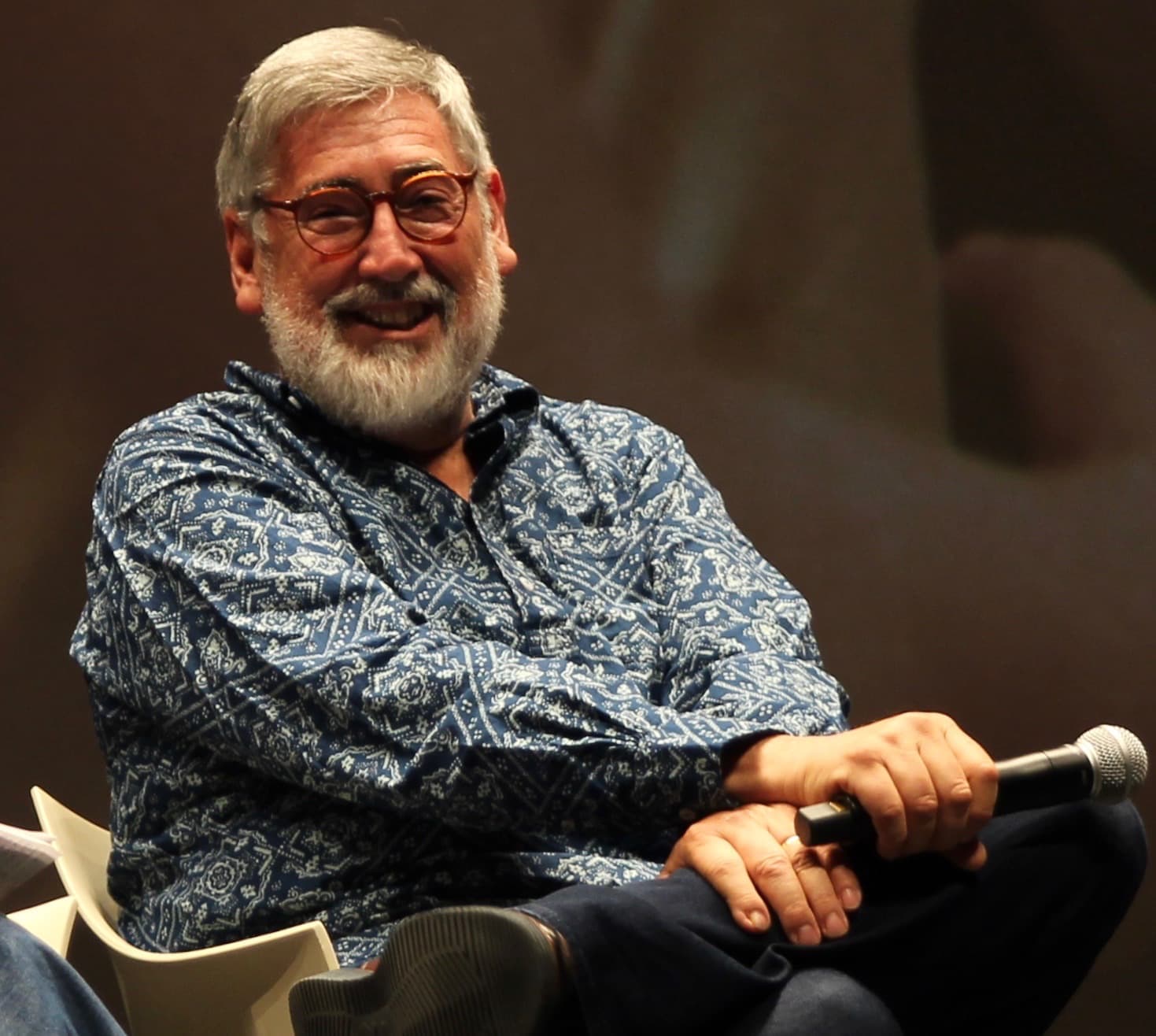 John Landis, white-bearded in glasses, seated on stage with a microphone