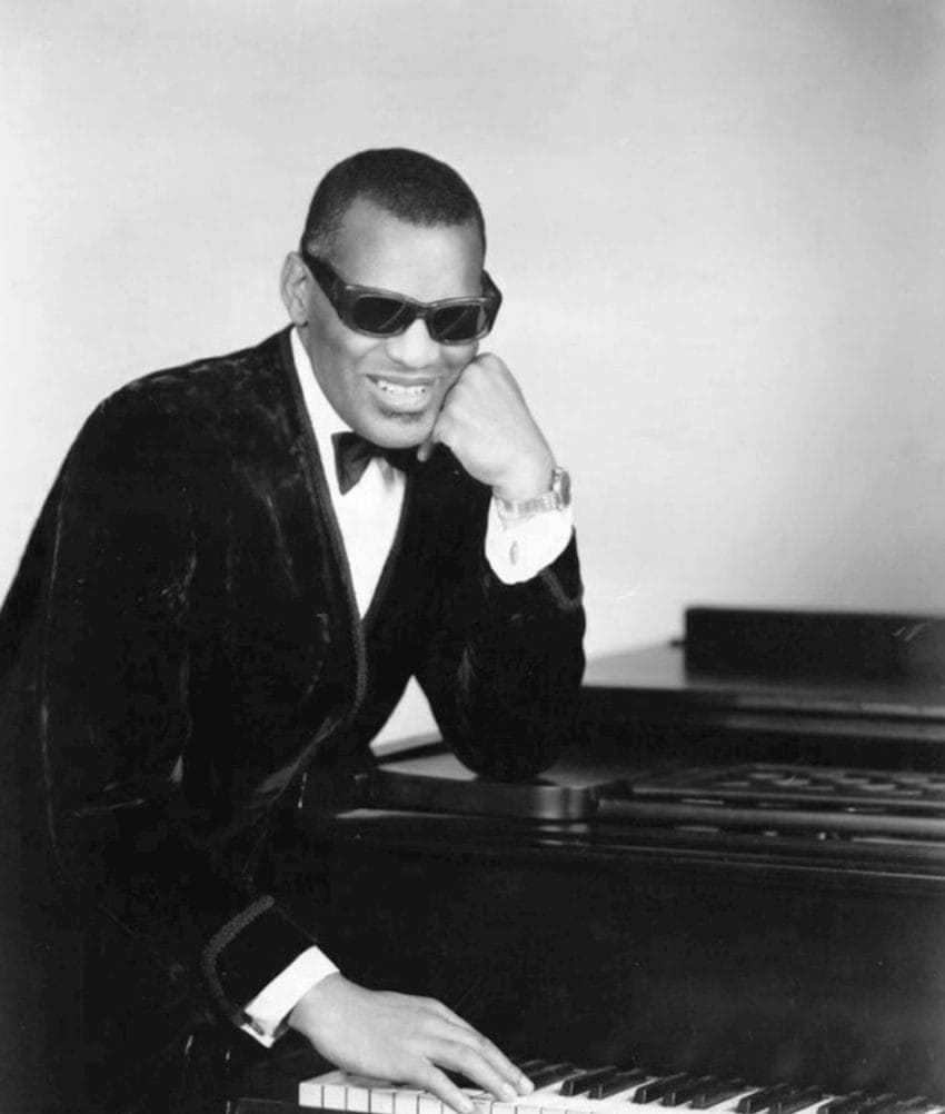 Ray Charles in dark glasses seated at a piano