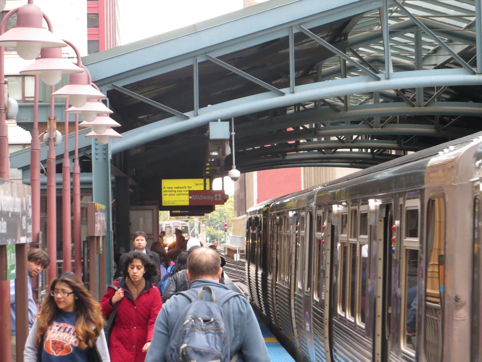 Passengers on an elevated L platform beside a train, under a steel canopy