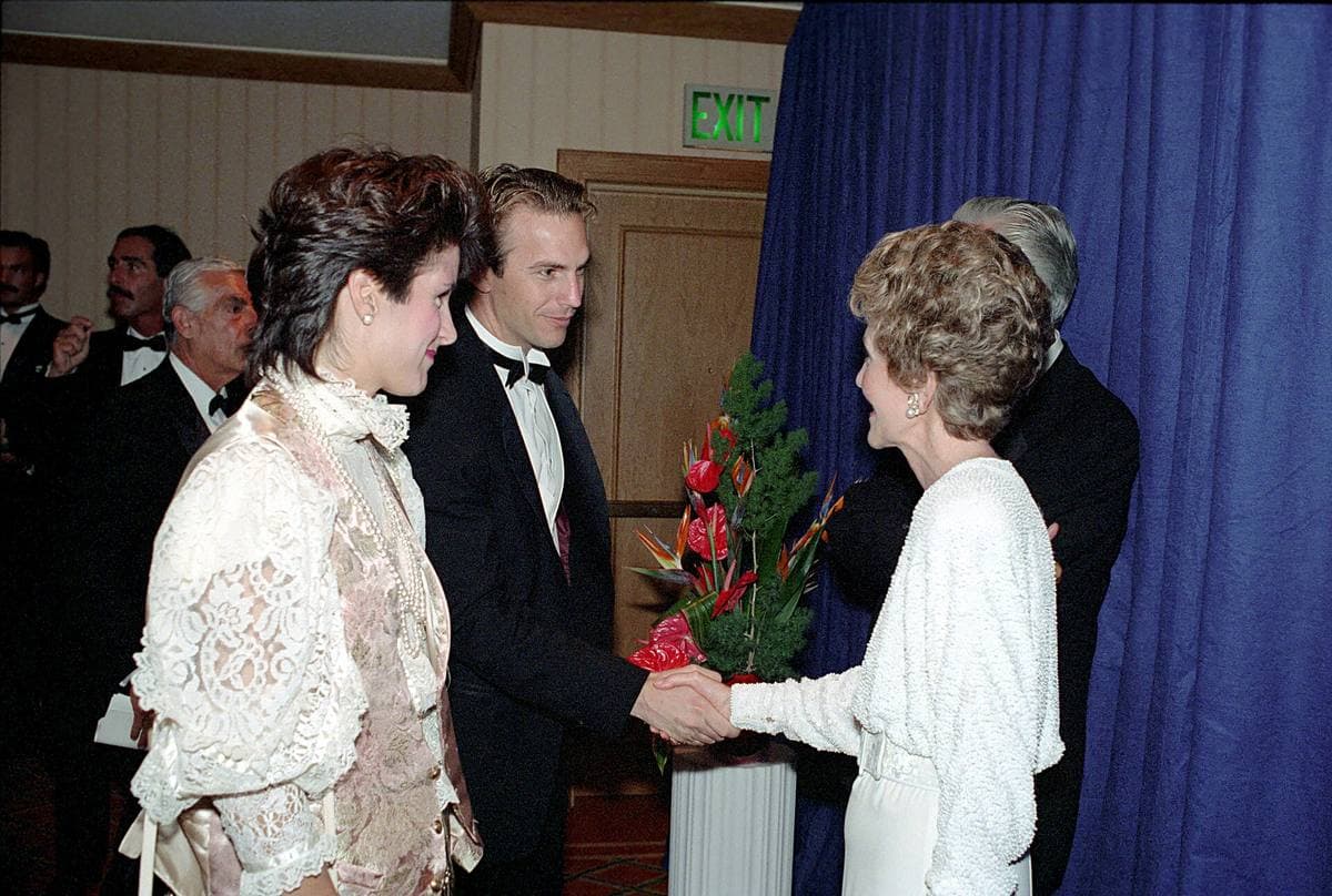 Kevin Costner in a dinner jacket shaking hands with Nancy Reagan at a formal dinner