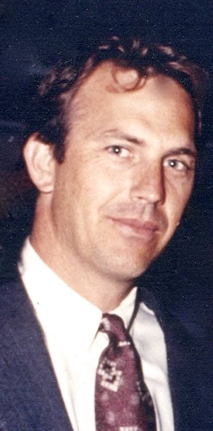 Kevin Costner smiling in a dark suit and patterned tie