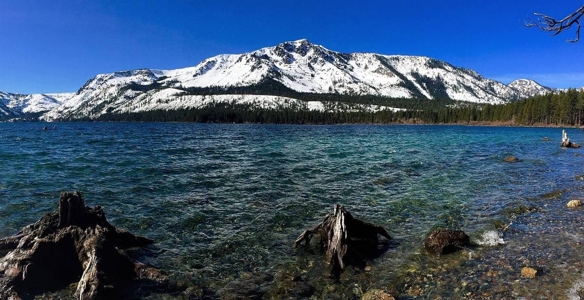 A clear blue mountain lake with snow on the peak behind