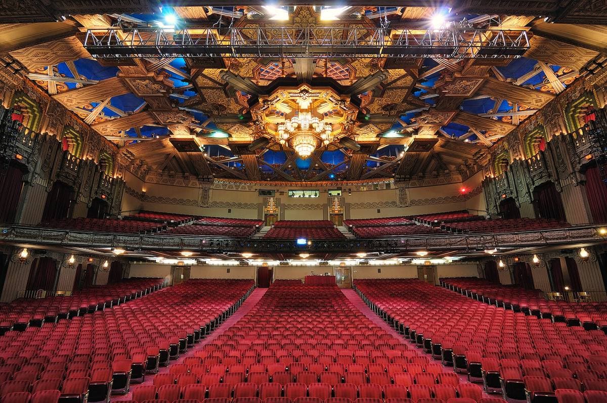 A gilded Art Deco theatre auditorium with red seats