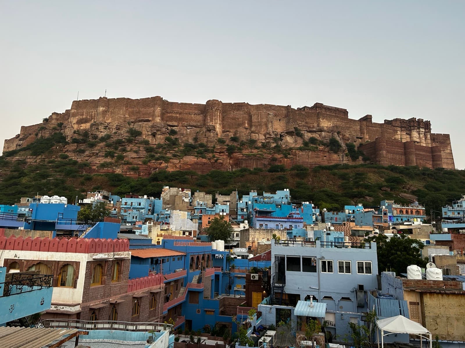 A fort on a ridge above a city of blue-painted houses in early light