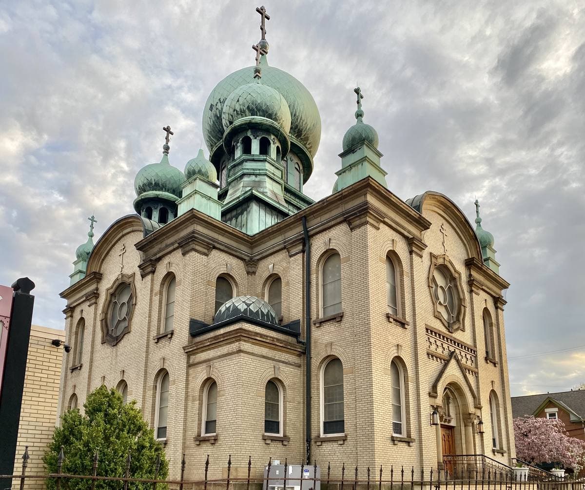 A cream brick cathedral with green copper onion domes under a cloudy sky