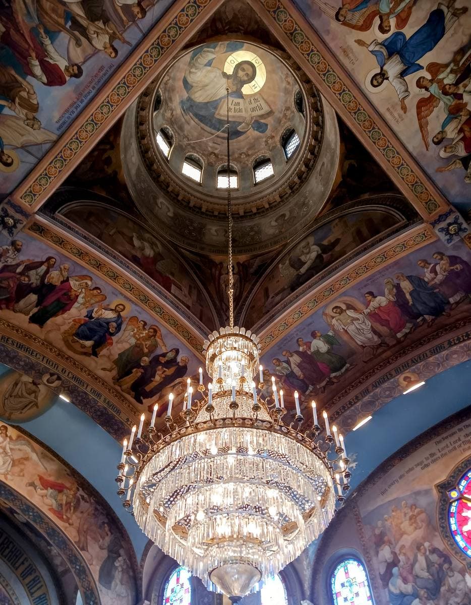 Looking straight up into a painted dome with a large crystal chandelier