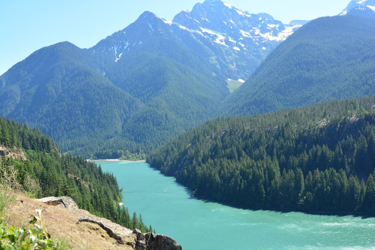 A turquoise lake between steep forested mountains with snow on the peaks