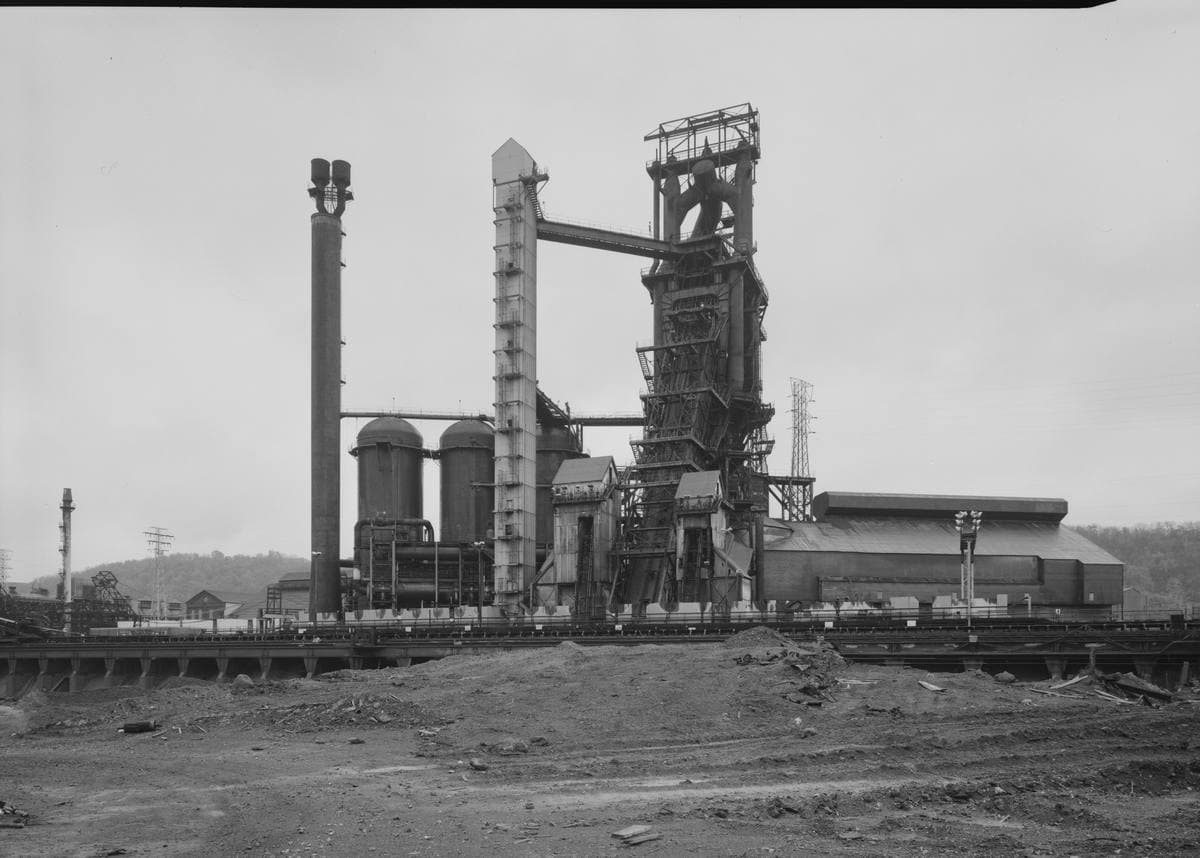 A black-and-white view of a tall blast furnace and stoves beside bare ground