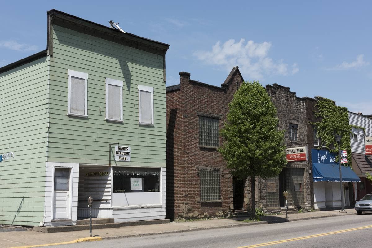 A pale green clapboard shop beside brick buildings on a small-town street