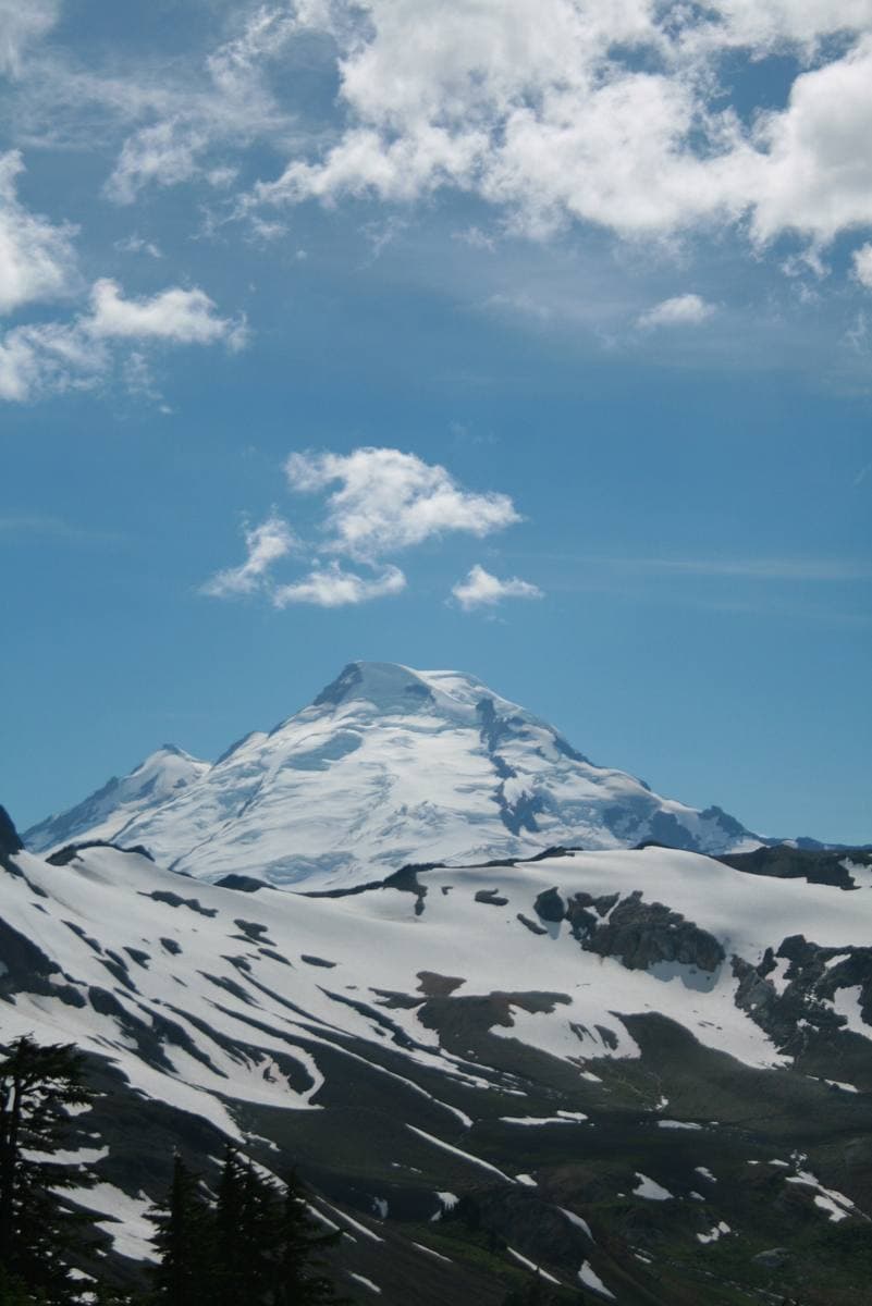 A snow-capped volcano above green slopes and white clouds