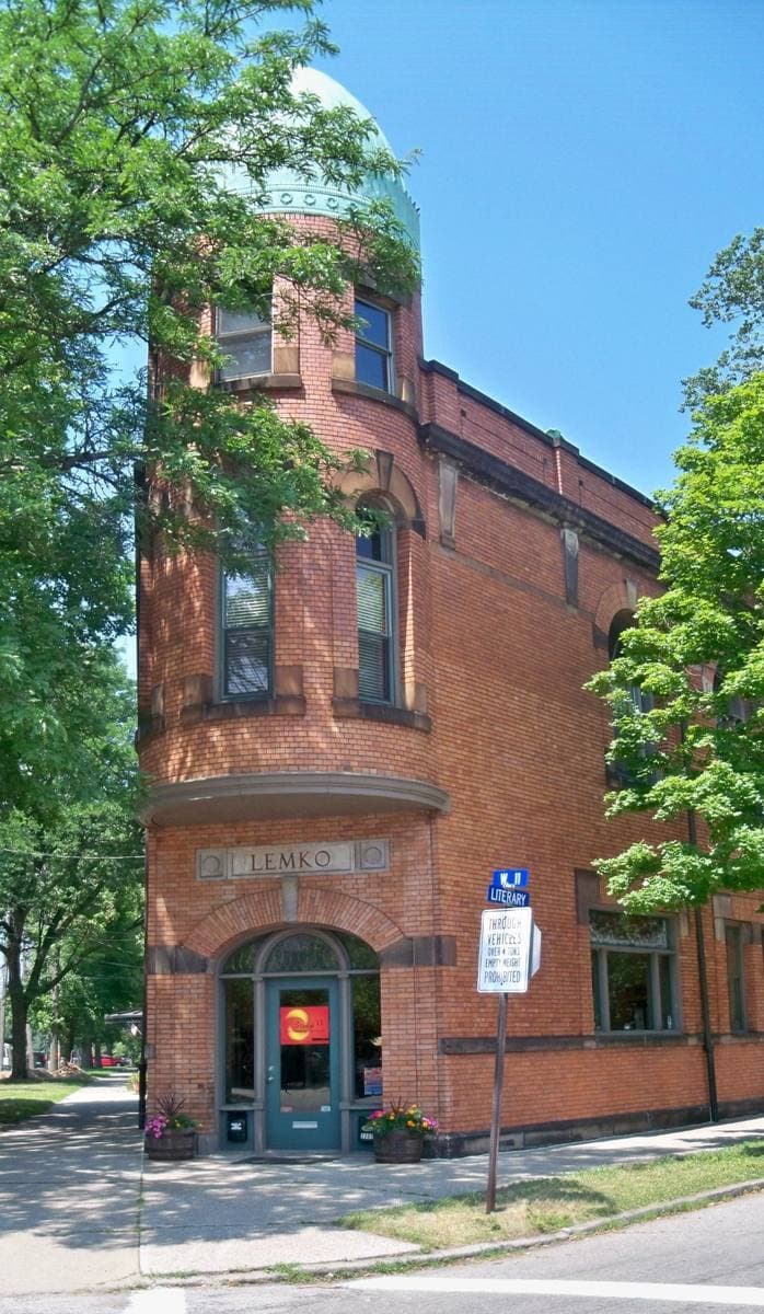A tall red-brick corner building with a turret corner and trees