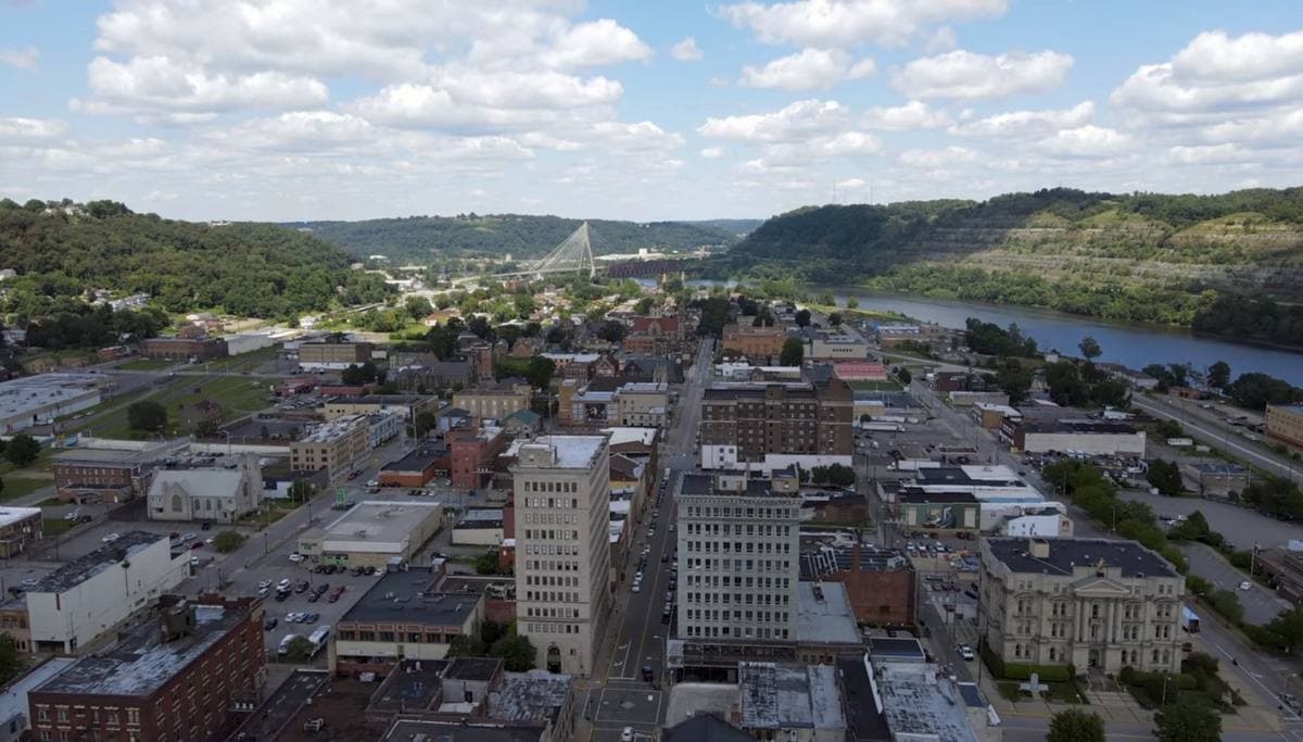 An aerial view of a small river city with green hills and a bridge