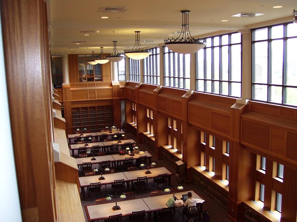 A long wood-panelled library with tall windows and rows of study desks below a balcony