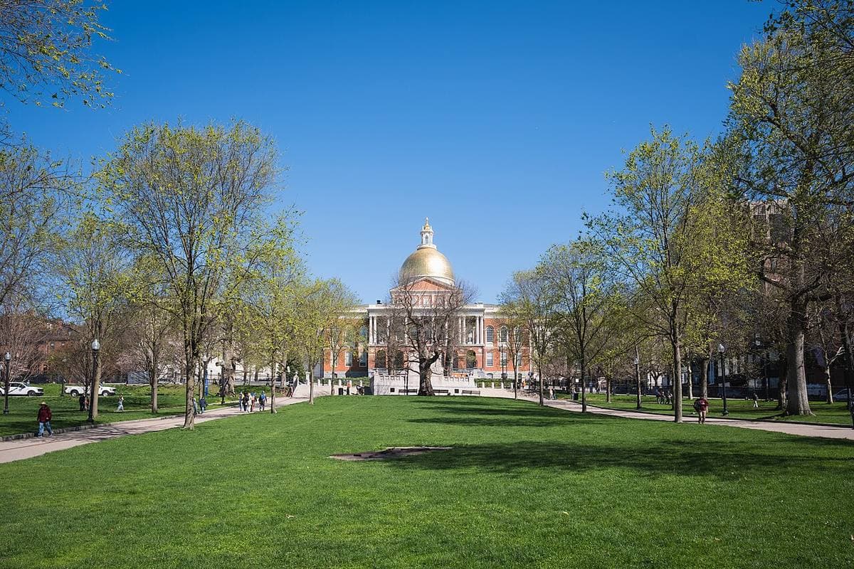 A gold-domed red-brick building at the top of a sloping lawn with trees
