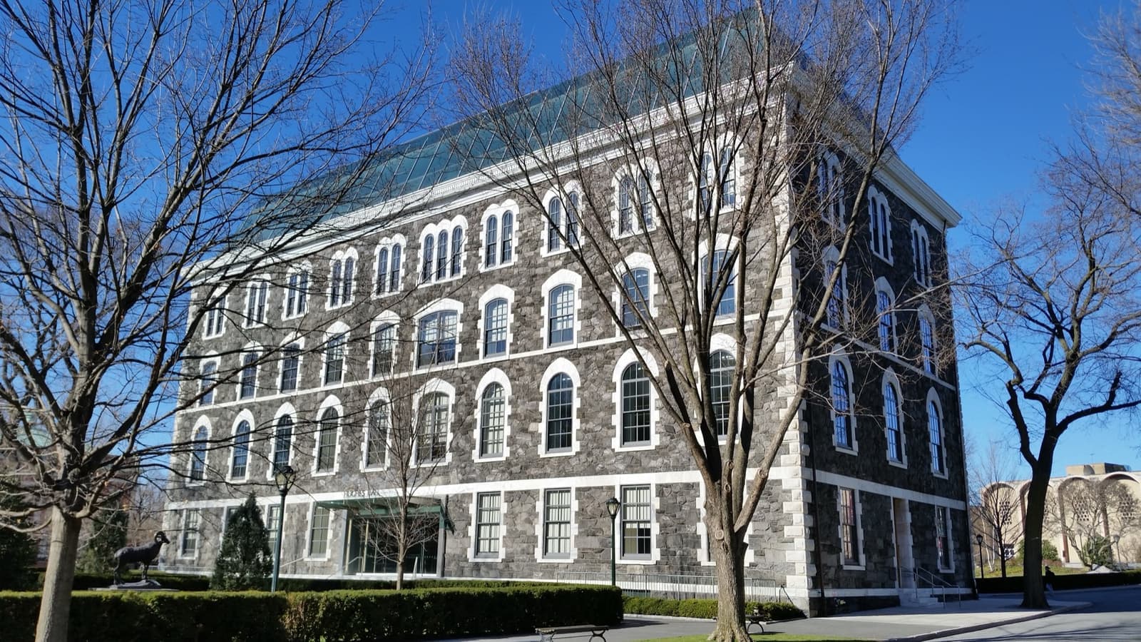 A grey stone collegiate building with a central tower and gabled windows