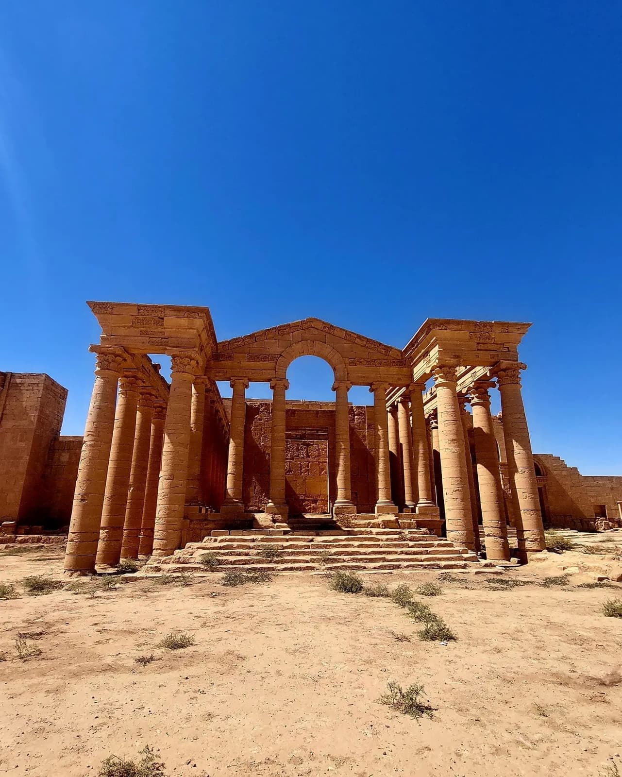 Weathered sandstone columns and a great central arch under a deep blue sky in the desert
