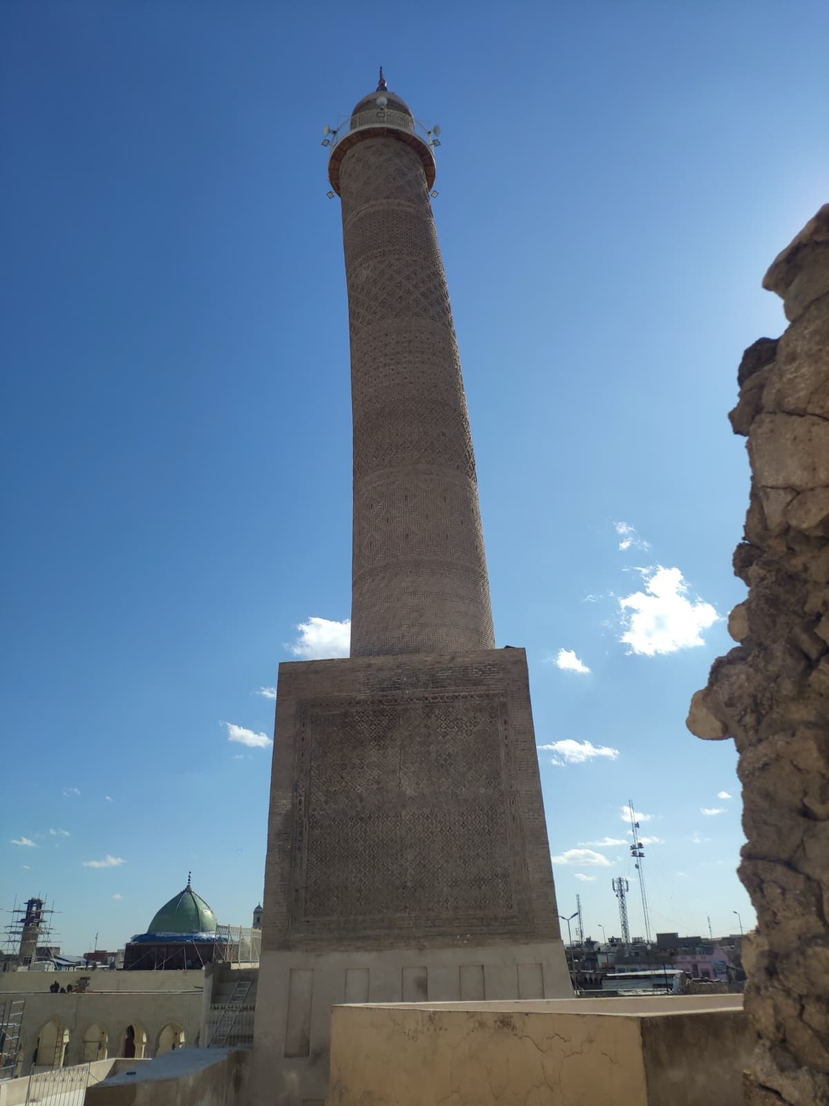 A tall brick minaret with patterned bands against a pale sky