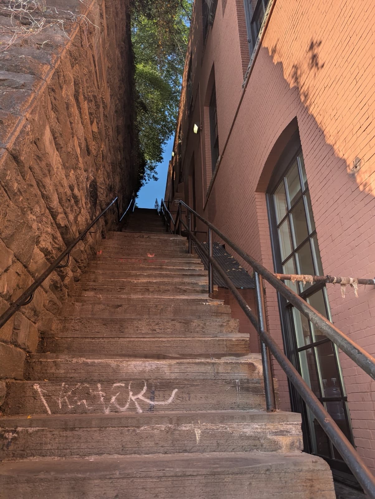 Steep stone steps in late sun between a stone retaining wall and a brick building