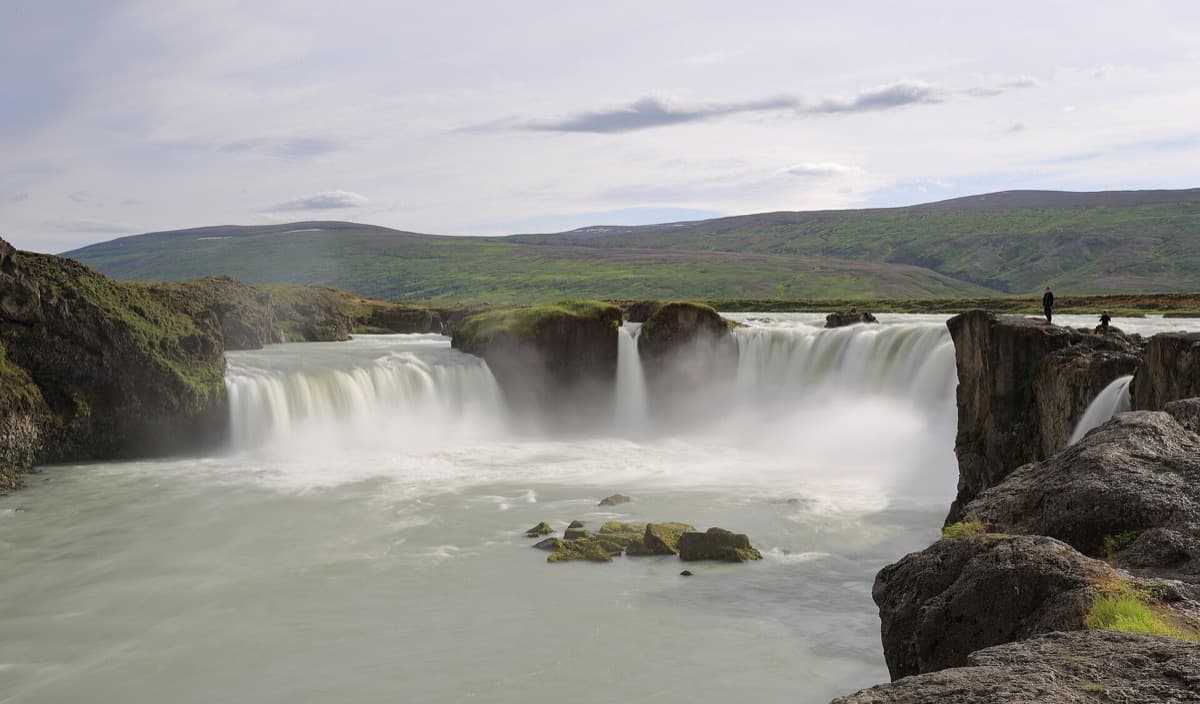 A wide waterfall pouring over a horseshoe cliff under a pale sky