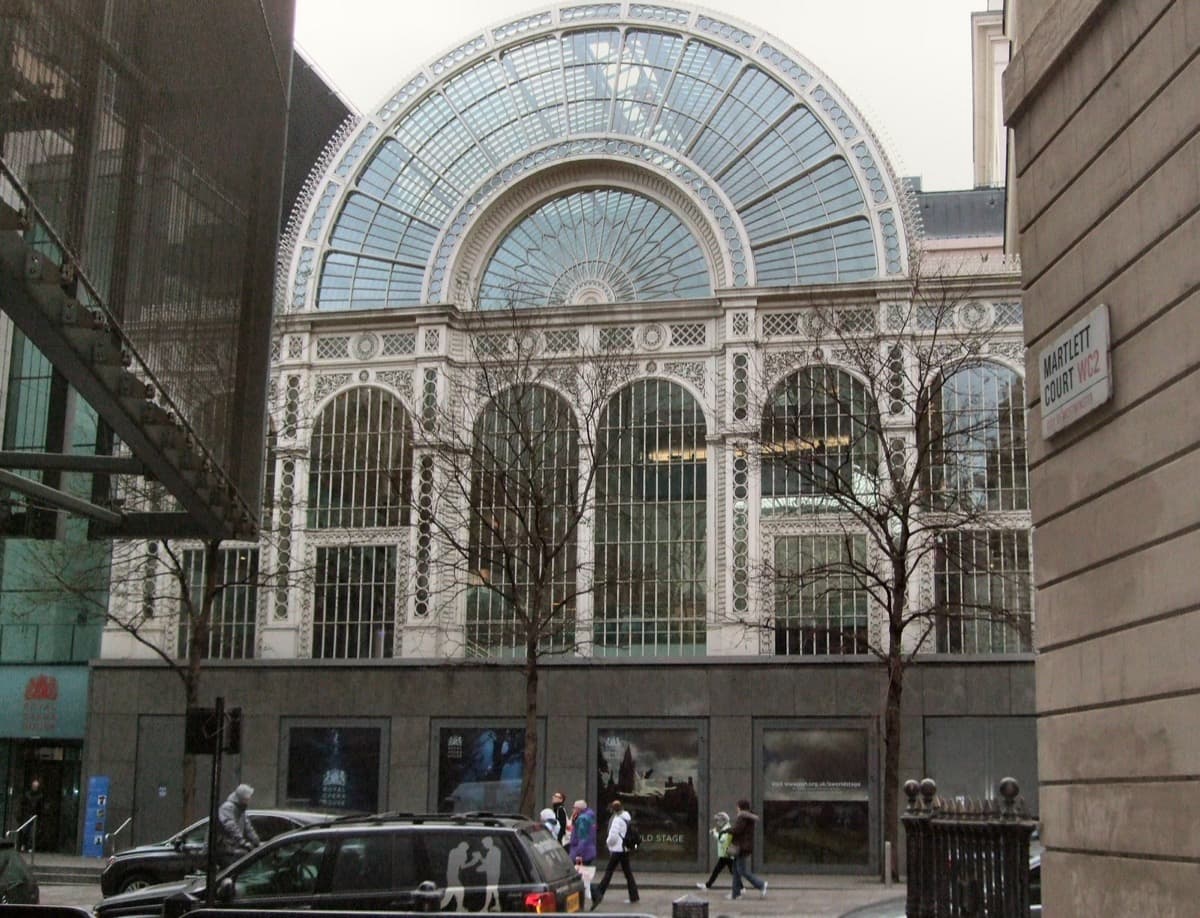 The columned portico and glass-and-iron front of the Royal Opera House on a London street