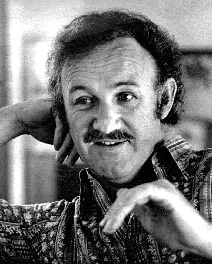 Black-and-white photograph of Gene Hackman smiling, chin resting on his hand