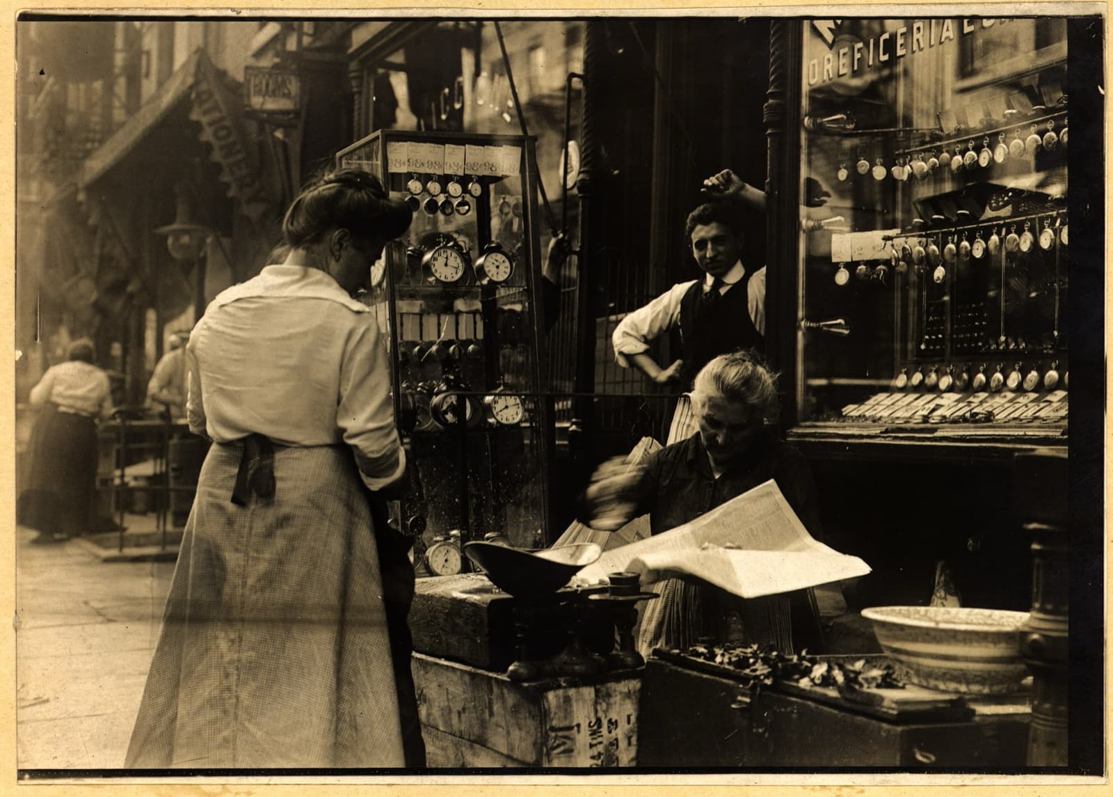 A shop front on Mott Street with goods hung in the window and people outside