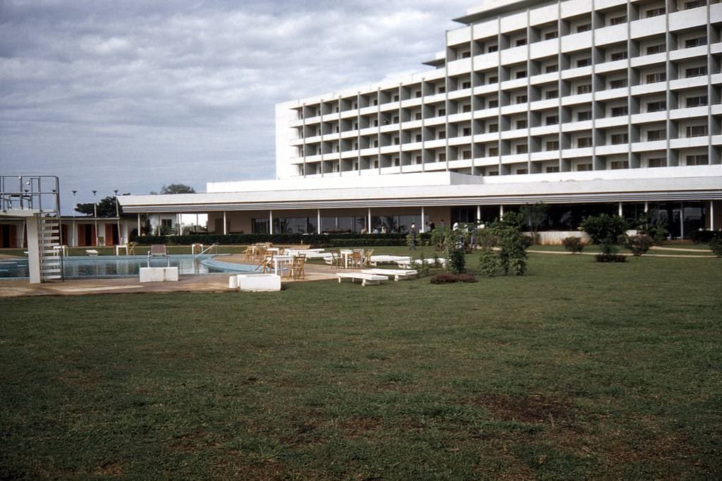 A long modern hotel block with rows of balconies behind lawns and palms