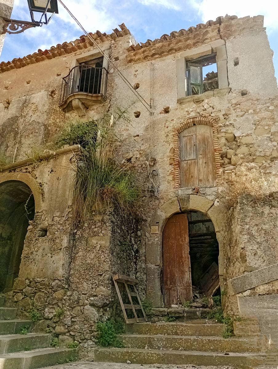 Old stone houses with arched doorways and worn steps in Forza d’Agrò