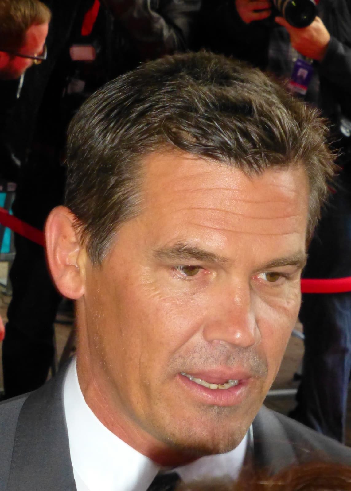 Josh Brolin in close-up at a premiere, in a dark suit and white shirt