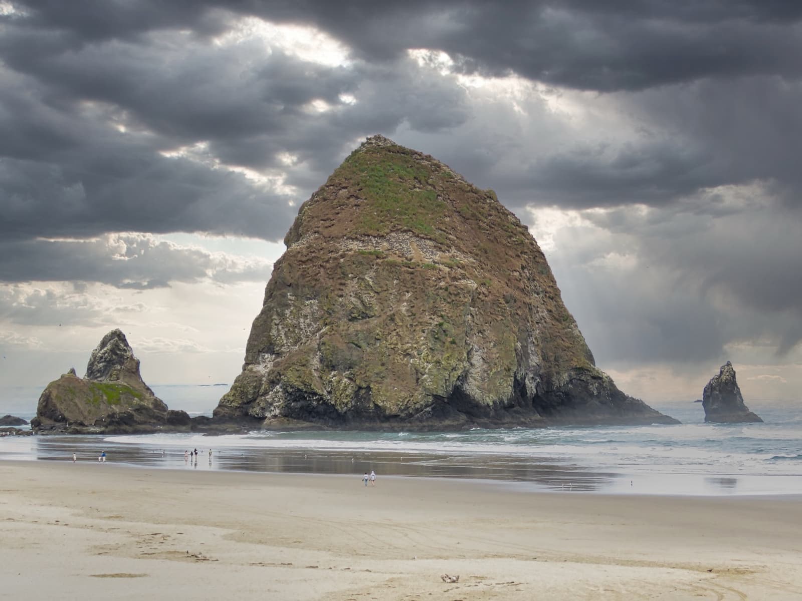 The great dome of Haystack Rock rising from wet sand under a stormy sky, two smaller rocks beside it