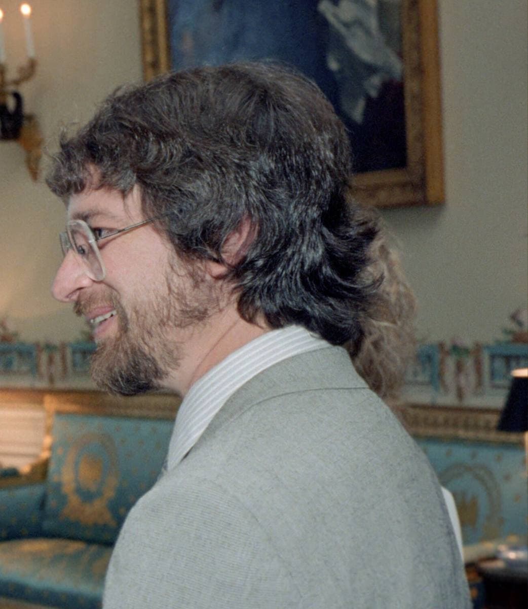 Steven Spielberg in 1982, bearded, in glasses and a grey jacket