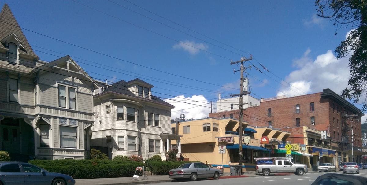 A Berkeley street with low buildings, trees and parked cars