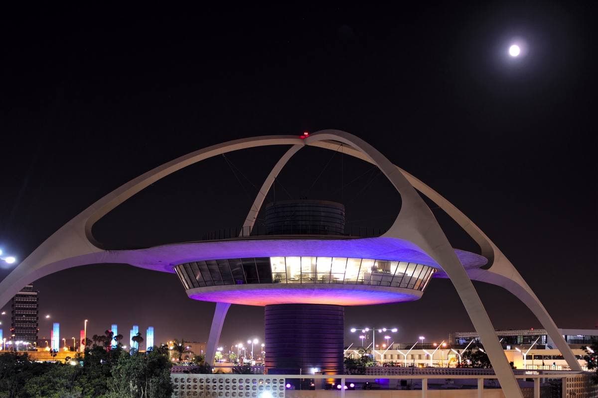 The arched white Theme Building at Los Angeles airport, lit at night with the moon above