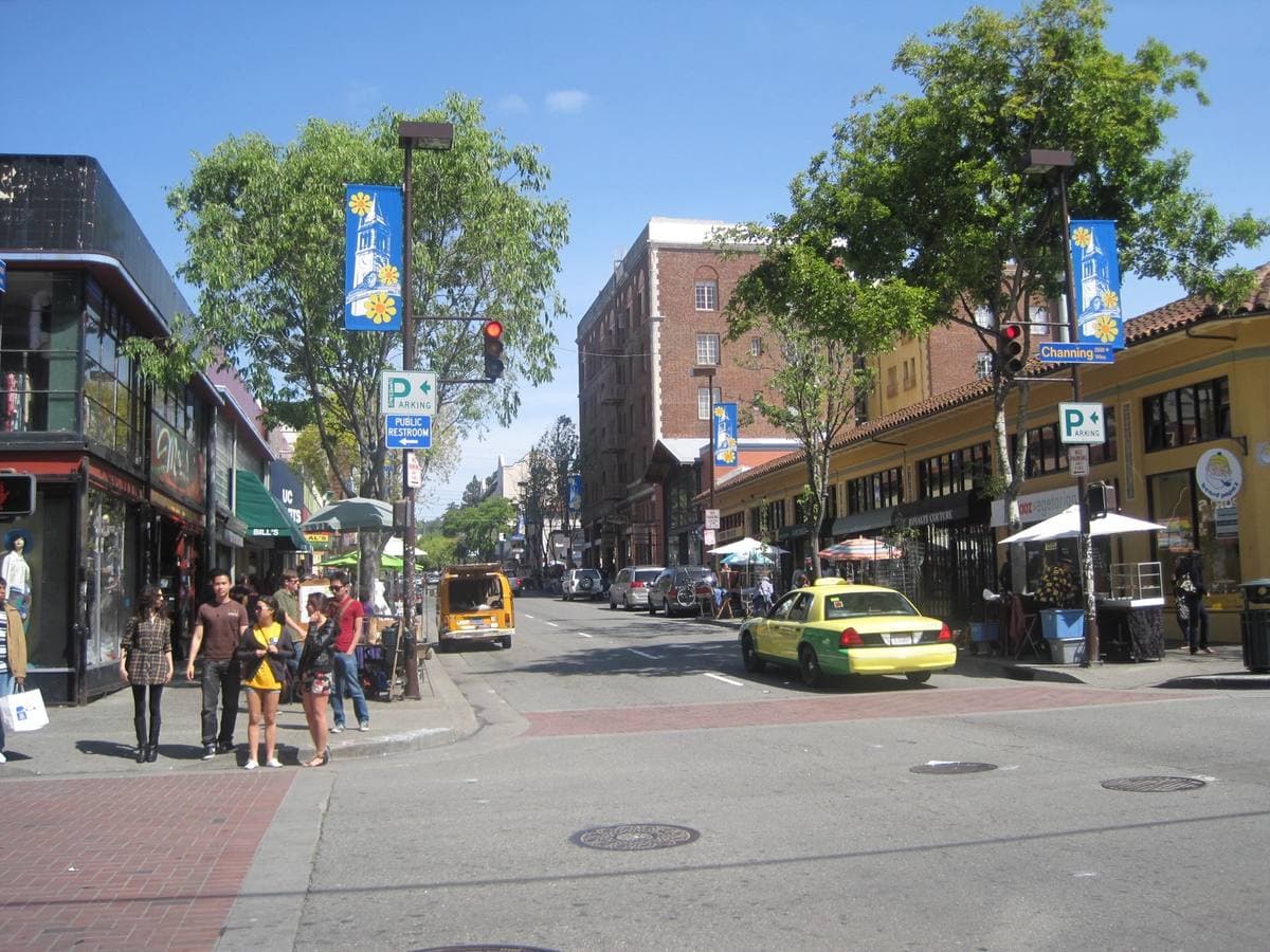 A busy street of shopfronts and pedestrians leading towards the university