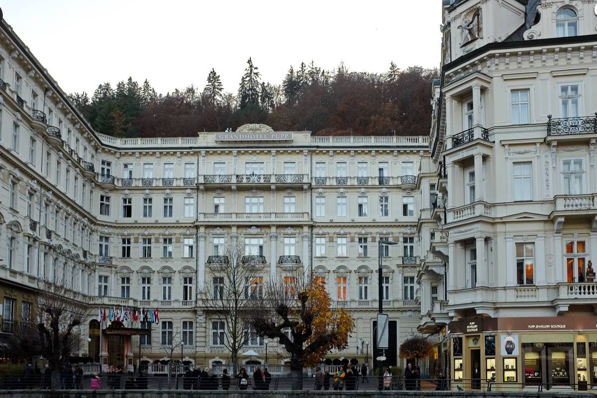 A long cream and white palace hotel with balconies and a domed centre, facing a square