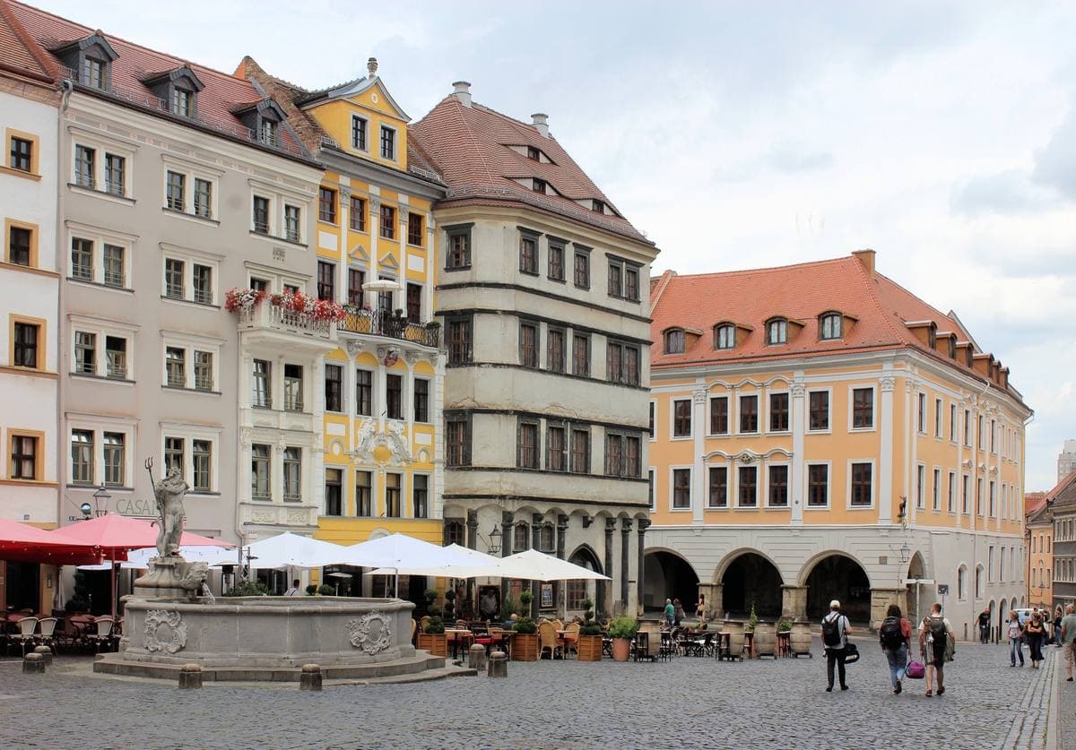 A cobbled square of tall Renaissance and Baroque houses with café umbrellas, the town hall tower behind