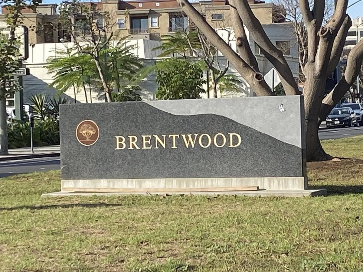 A stone sign reading Brentwood on a grass verge, a tree and buildings behind