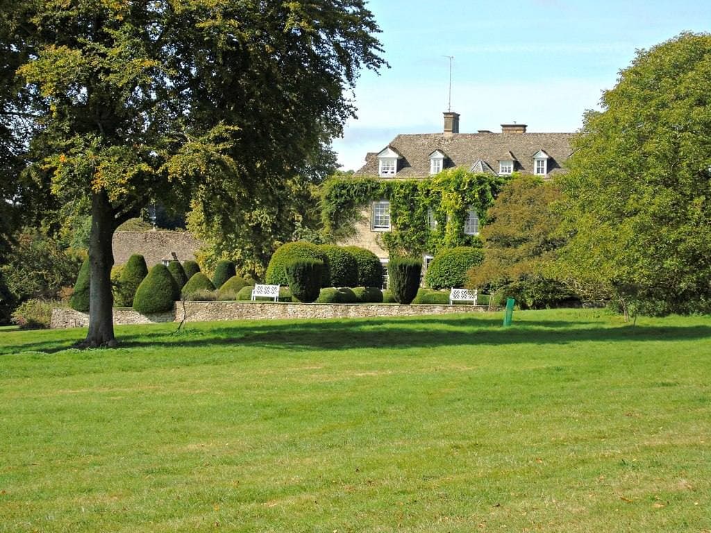 An ivy-covered stone manor house glimpsed past a wide lawn and clipped yew