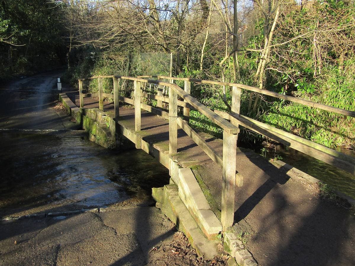 A low timber footbridge with handrails crossing a shallow stream under bare trees