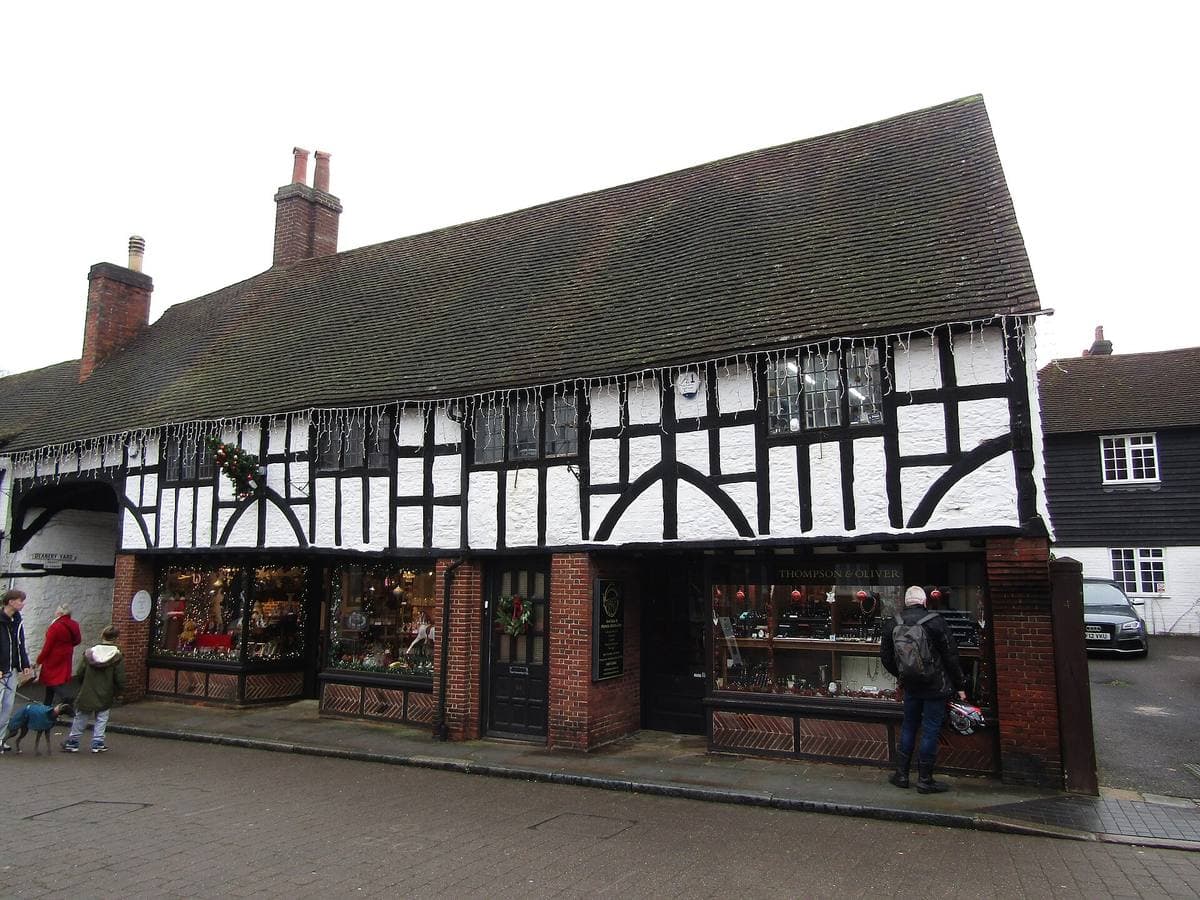 A long black-and-white timber-framed building with shopfronts on a narrow street