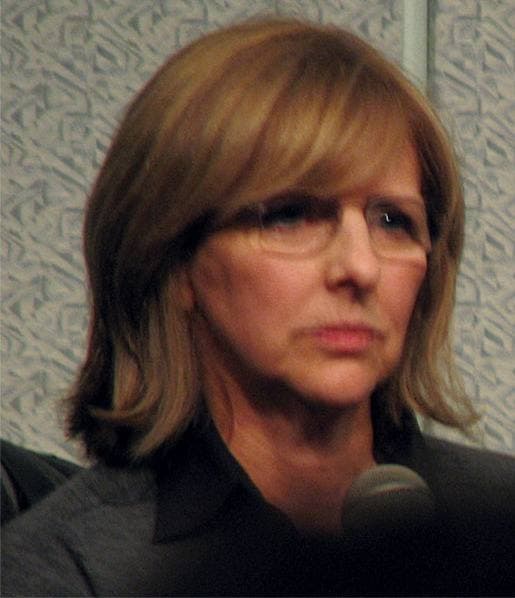 Nancy Meyers, shoulder-length hair and glasses, listening at a microphone