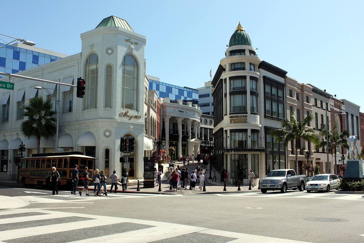 A wide street crossing with white shop buildings and palm trees in Beverly Hills