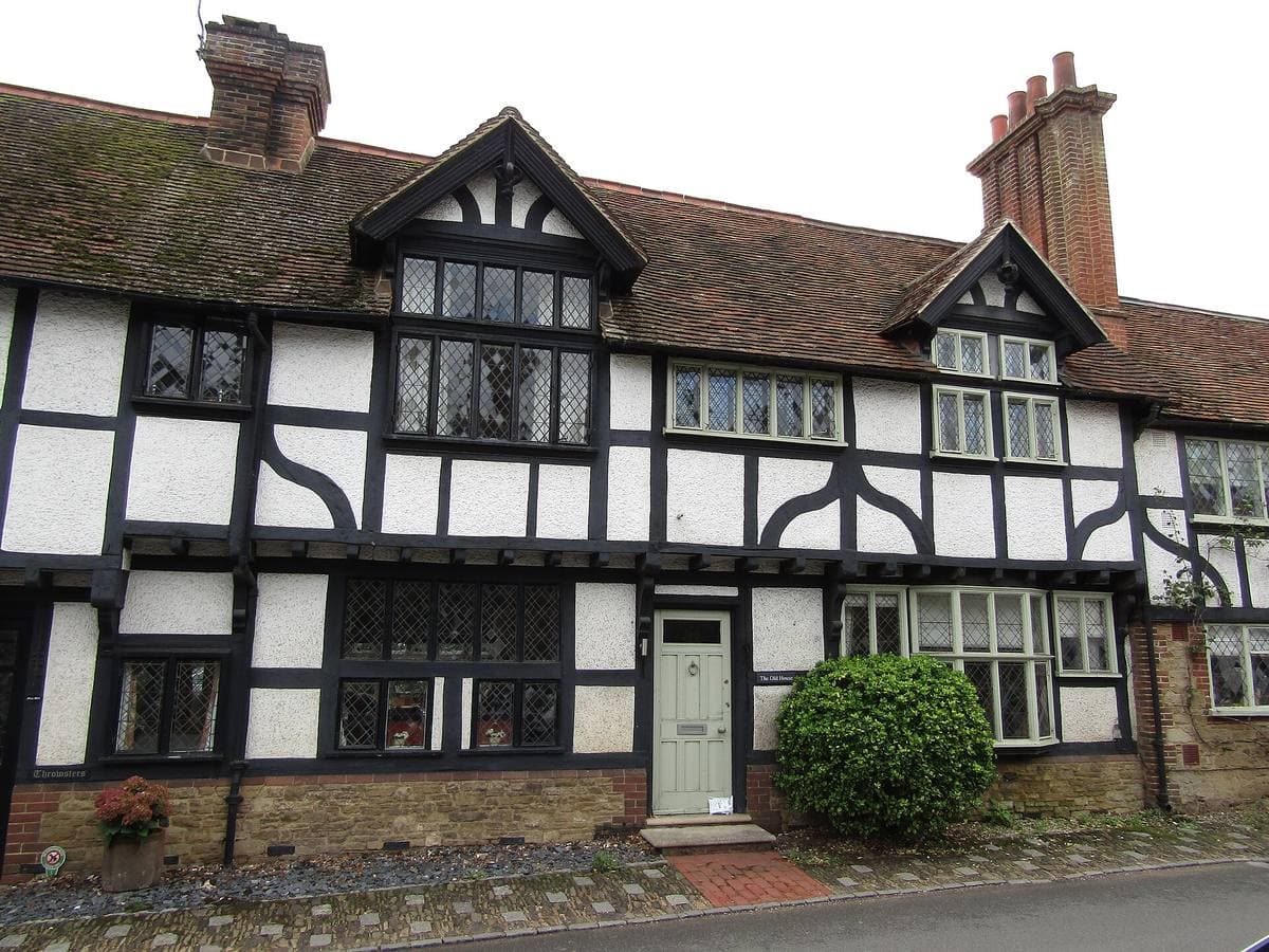 A timber-framed row of cottages with tall chimneys on a village street