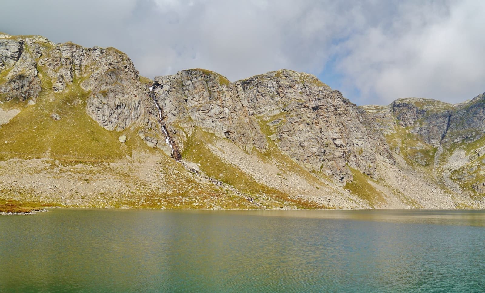 A green alpine lake under steep rocky slopes