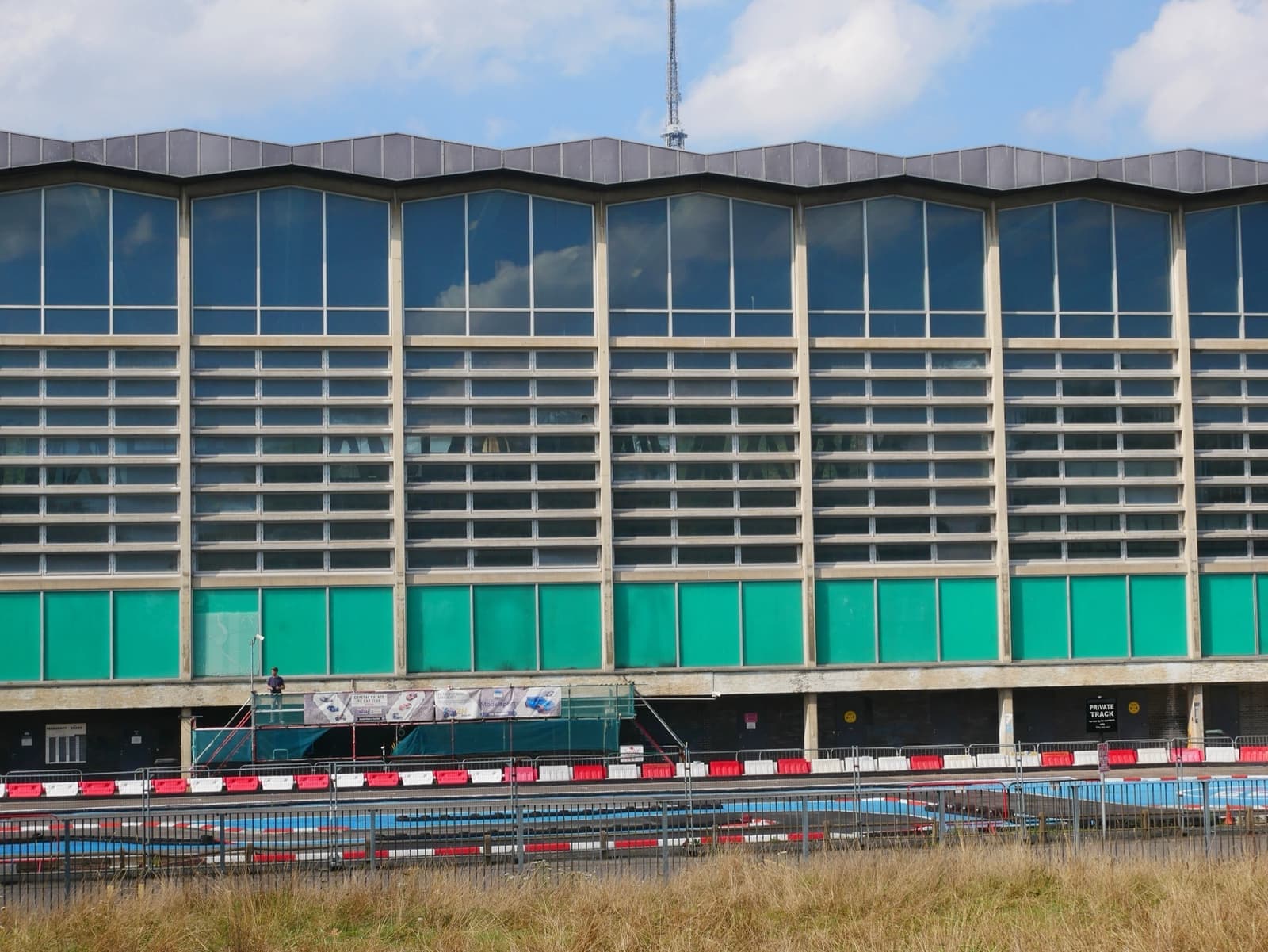 A long glass-fronted 1960s sports building with a green band at ground level
